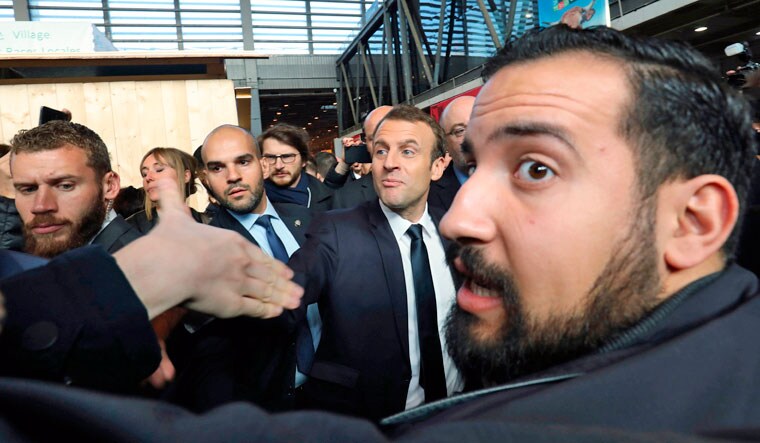 [File] French president Emmanuel Macron (C) shakes hands with people as former Elysee senior security officer Alexandre Benalla (R) looks on | AFP