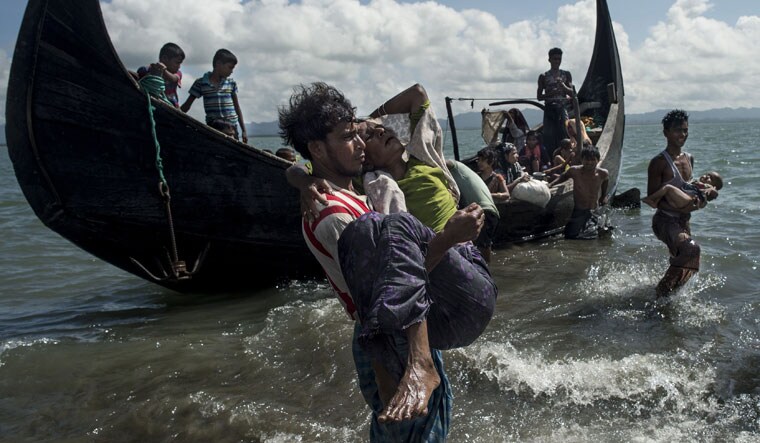 (FILE) A Bangladeshi man helps Rohingya Muslim refugees to disembark from a boat on the Bangladeshi shoreline of the Naf river after crossing the border from Myanmar | AFP