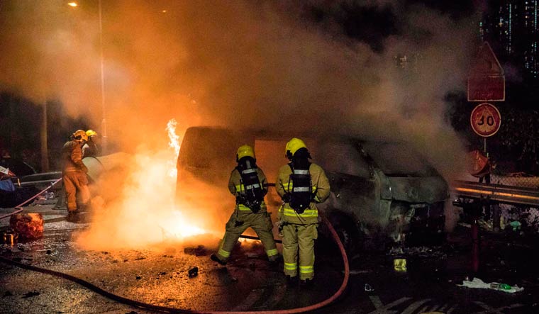 Firemen put out a fire in a van, part of a barricade, after protesters set it alight near the Chinese University of Hong Kong | AFP