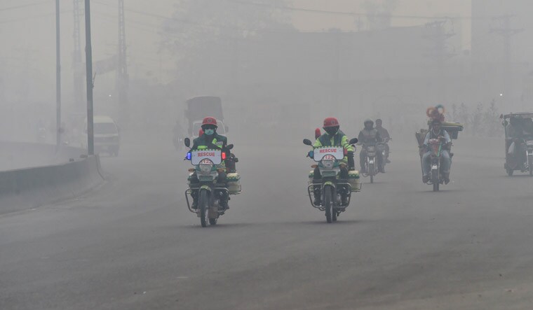 Rescuers ride motorcycles on a road amid the heavy smog condition in Lahore | AFP
