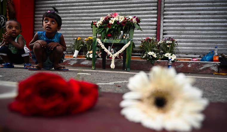Children sit next to flowers left by mourners near St. Anthony's Shrine in Colombo on April 23, two days after a series of bomb blasts targeting churches and luxury hotels in Sri Lanka | AFP