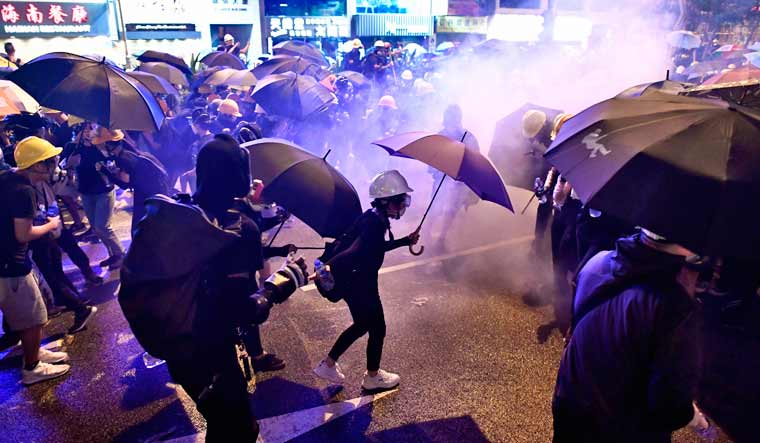 Protesters hold umbrellas as they are enveloped by tear gas on a street during a demonstration against a controversial extradition bill in Hong Kong | AFP