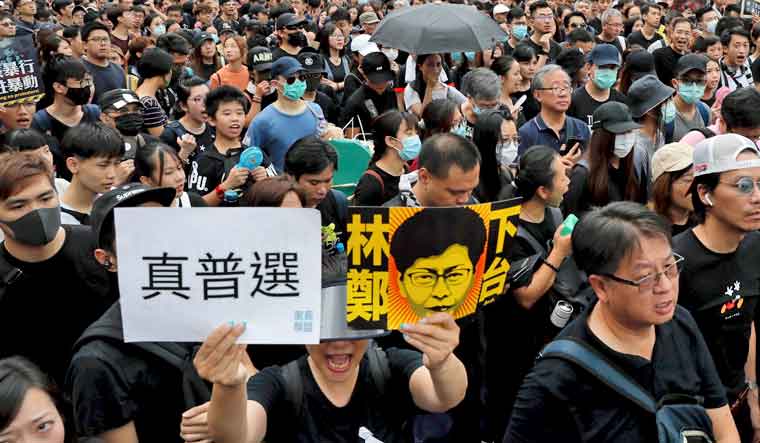 Protesters take part in a march holding a caricature of Hong Kong Chief Executive Carrie Lam with the words "Step Down" | AP