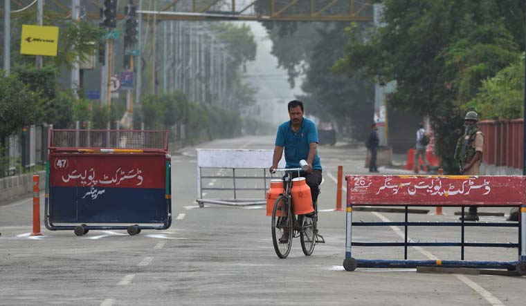 A man rides a bicycle with milk containers on a deserted road during security lockdown in Srinagar | AFP
