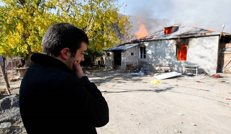 A man stands near a house set on fire by departing Ethnic Armenians, in an area which had held under their military control but is soon to be turned over to Azerbaijan, in the village of Cherektar in the region of Nagorno-Karabakh | AP