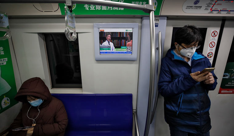 Masked commuters ride in a subway train in Beijing as a monitor shows a doctor talking about precautions against COVID-19 virus | AP