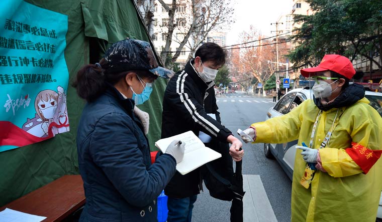 A man wearing a face mask has his temperature checked before entering a locked down residential area in Wuhan in central China's Hubei Province | AP