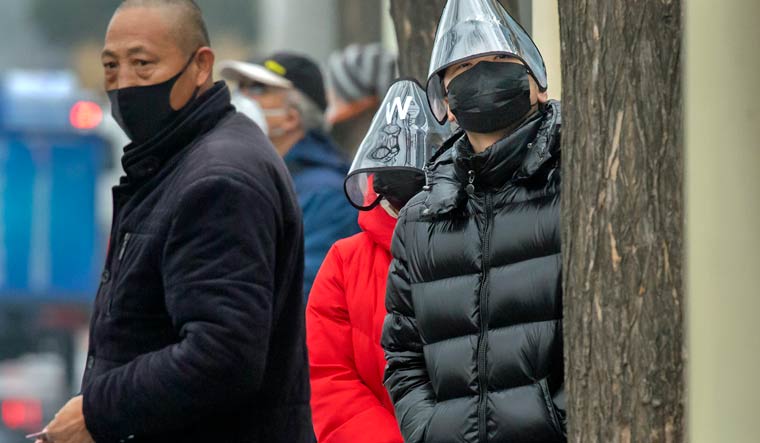 A man wears a plastic face shield as he waits for a bus at a bus stop in Beijing, China | AP