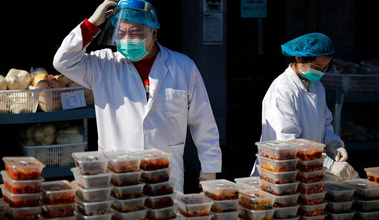 Workers wearing protective face masks prepare food orders outside a restaurant only offering take-out business in Beijing | AP