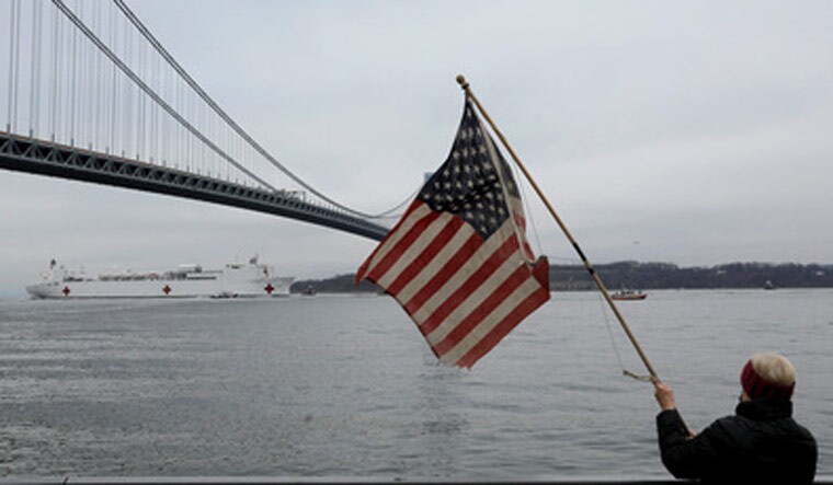A person waves a United States flag as the USNS Comfort passes under the Verrazzano-Narrows Bridge as it enters New York Harbor during the outbreak of the coronavirus disease (COVID-19) in New York City | Reuters