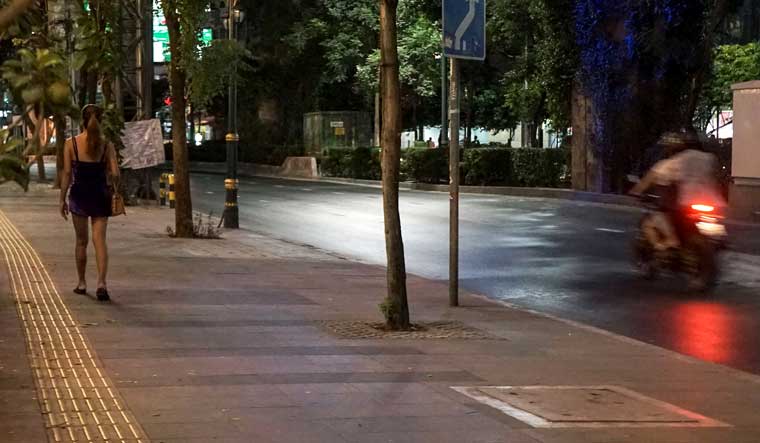 Motorists driving on an empty road past a woman (L) working in the sex trade in Bangkok, in an area usually busy with sex workers but now closed as authorities seek to halt the spread of the COVID-19 coronavirus | Aidan JONES / AFP