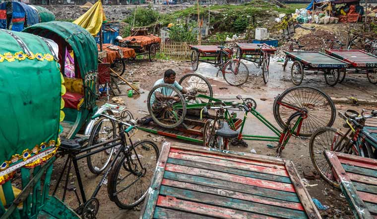 A labourer repairs a tricycle rickshaw at a garage in Dhaka | AFP