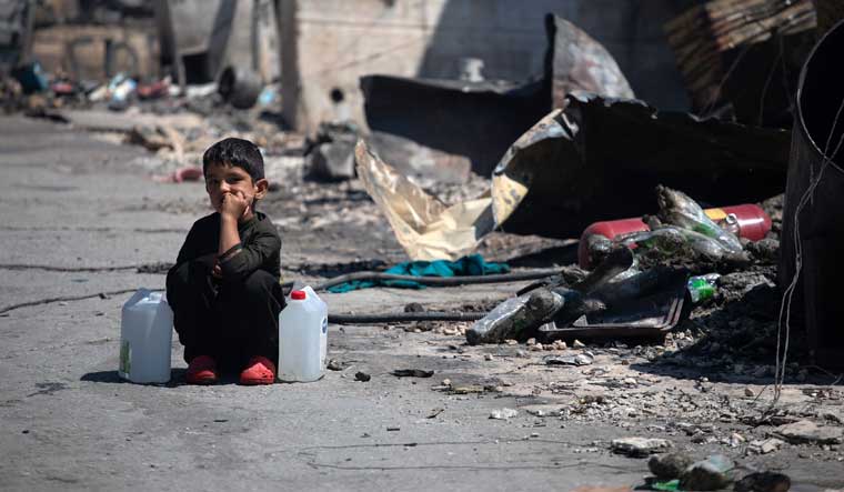 A boy with two water cans sits next to destroyed shelters following a fire at the Moria camp for refugees and migrants on the island of Lesbos, Greece, September 9, 2020 | REUTERS/Alkis Konstantinidis
