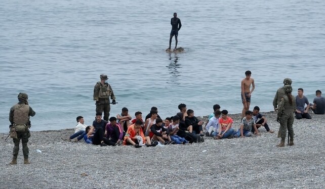 Spanish legionnaires stand around Moroccan citizens, after thousands of Moroccans swam across Spanish-Moroccan border on Monday, in Ceuta | Reuters
