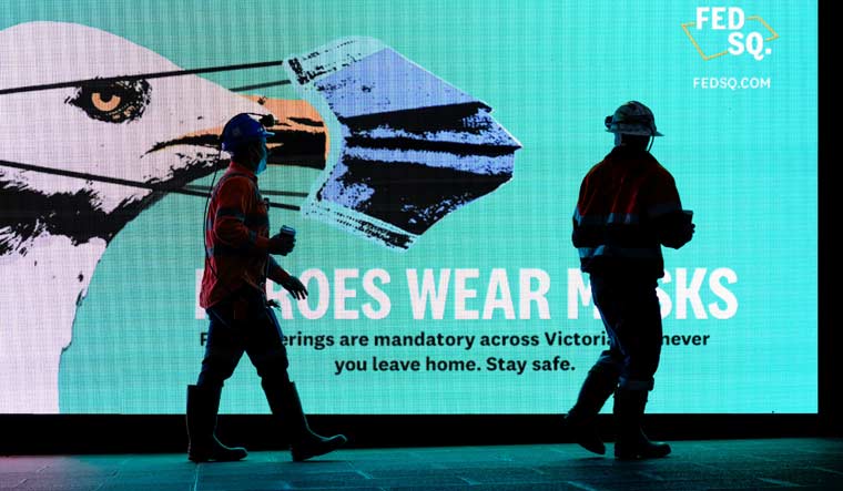 FILE PHOTO: Essential workers walk past a 'Heroes Wear Masks' sign on the first day of a seven-day lockdown as the state of Victoria looks to curb the spread of a coronavirus disease (COVID-19) outbreak in Melbourne, Australia, May 28, 2021. REUTERS/Sandra Sanders/File Photo
