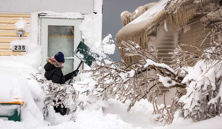 A woman shovels snow beside a house and downed tree coated in ice formed by the spray of Lake Erie during a winter storm in Hamburg, New York | Reuters