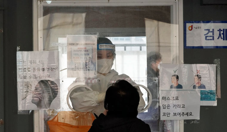 A medical worker in a booth takes a nasal swab sample from a woman at a makeshift testing site in Seoul, South Korea, Tuesday, March 15, 2022 | AP