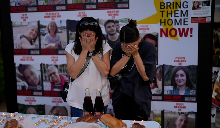 Two women pray next to photographs of people who were abducted during the Hamas attack on Israel | AP