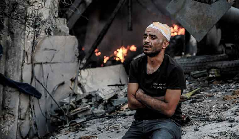 An injured man sits in front of a smouldering building in the aftermath of an Israeli strike on Gaza City | AFP