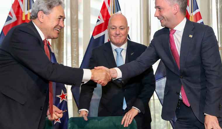 New Zealand Prime Minister elect Christopher Luxon, centre, watches as his coalition partners, New Zealand First leader Winston Peters, left, and ACT leader David Seymour shake hands following a signing ceremony in Wellington, New Zealand | AP