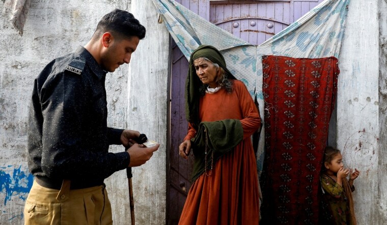 An Afghan citizen stands at the entrance of her house as a Pakistani police officer checks her registration card. | Reuters