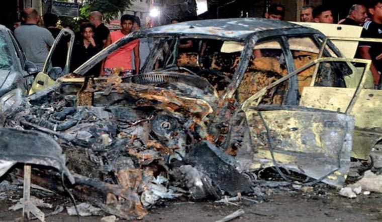 People stand near a damaged vehicle at the site of a bomb blast, outside the Sayeda Zeinab shrine city south of the Syrian capital Damascus, Syria July 27, 2023 | Reuters