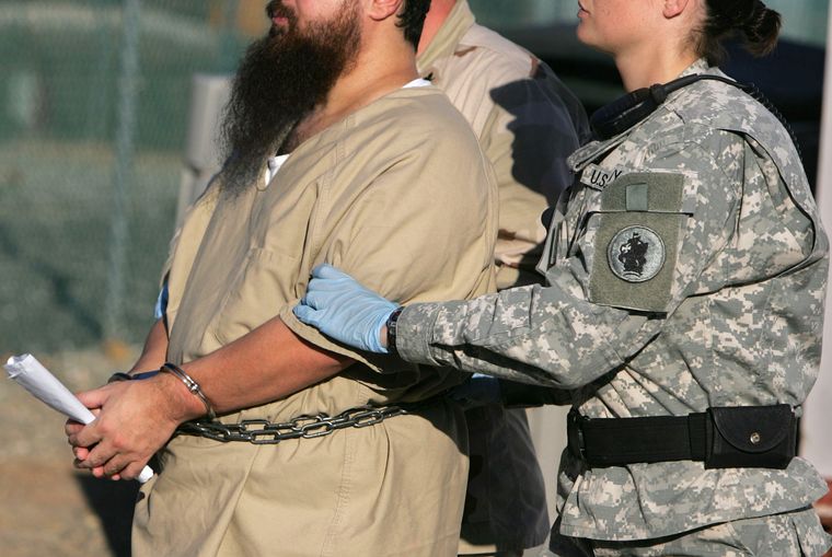 A detainee is escorted by a female guard after his annual administrative review board hearing at Camp Delta on December 6, 2006 | AP