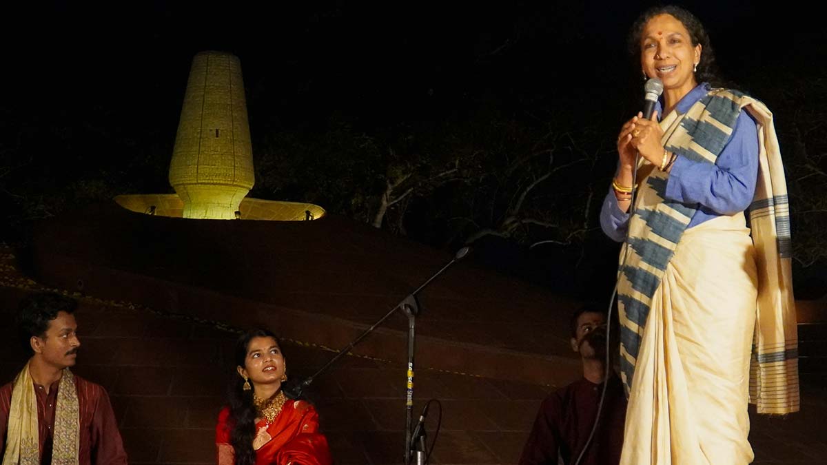 Spirit of devotion: Singer and Bihar MLA Maithili Thakur (in red sari) looks on as Jayanti S. Ravi, secretary of the Auroville Foundation, speaks during the Bhajan Sandhya at the Global Spirituality Mahotsav | Auroville Foundation