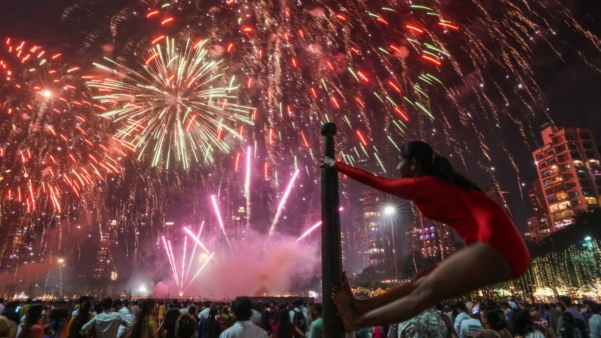 A girl performs on a mallakhamb pole as fireworks light up the sky during the festival of lights Diwali in Mumbai, India, on Oct. 20, 2025 | AP