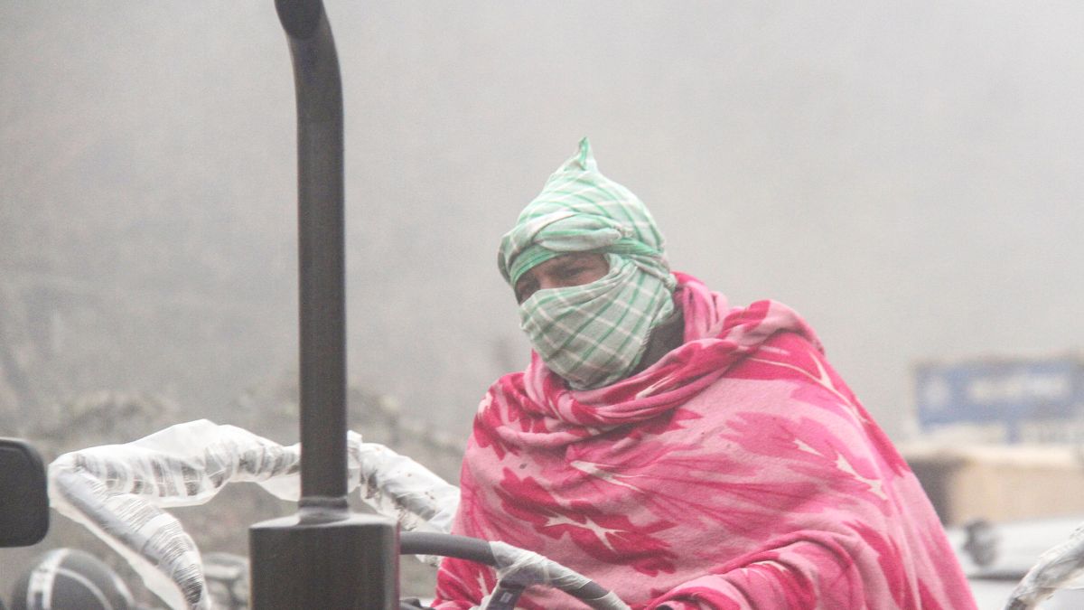 A man covers his face and wears blankets and gloves to shield himself from the cold as he drives a tractor on a foggy winter morning, in Gurugram | PTI