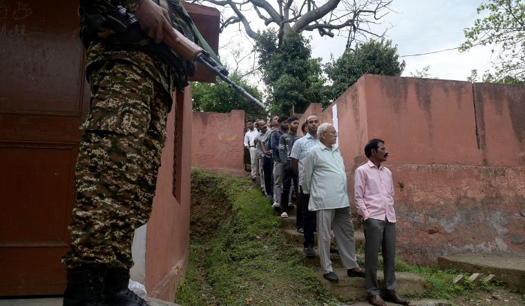 A security personnel stands guard beside people in a queue waiting to cast their votes at a polling station in Udhampur district, Jammu and Kashmir, on April 19, 2024 | AFP
