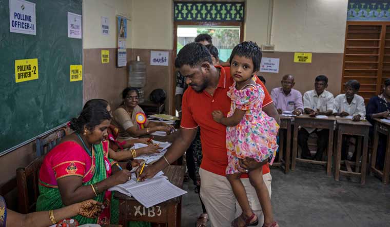 A voter carries a little girl as he casts his vote at a polling station during the first round of polling of Lok Sabha elections in Chennai | AP