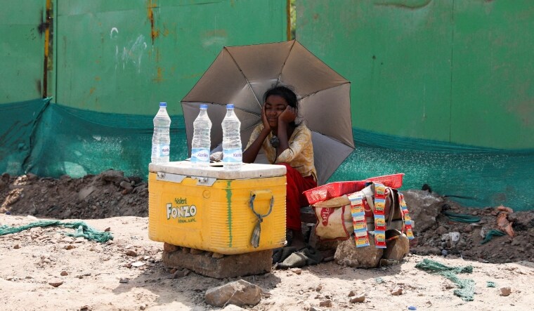 A girl selling water uses an umbrella to protect herself from the sun as she waits for customers on a hot summer day | Reuters