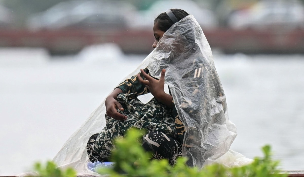 A girl wraps herself with plastic sheet during a light rain shower | AFP