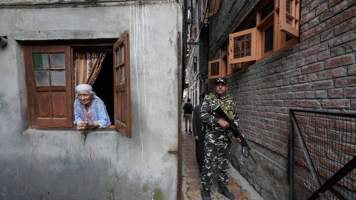 [File] An elderly Kashmiri woman looks on as a paramilitary soldier guards during the door-to -door campaigning by political parties for the assembly elections, in Srinagar | AP