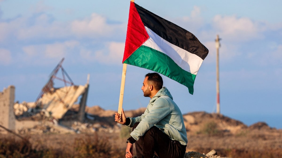 A man holds a Palestinian flag as he watches displaced Gazans crossing the Netzarim corridor from the southern Gaza Strip | AFP