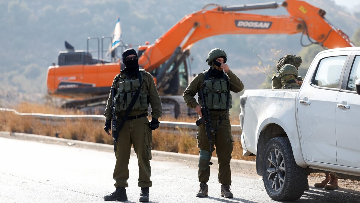 Israeli soldiers stand guard during the construction of a bypass road | Reuters