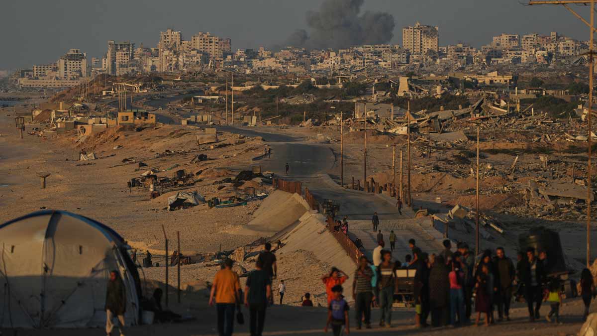 Displaced Palestinians walk along the coastal road, backdropped by smoke rising into the sky after an Israeli military strike in Gaza City | AP