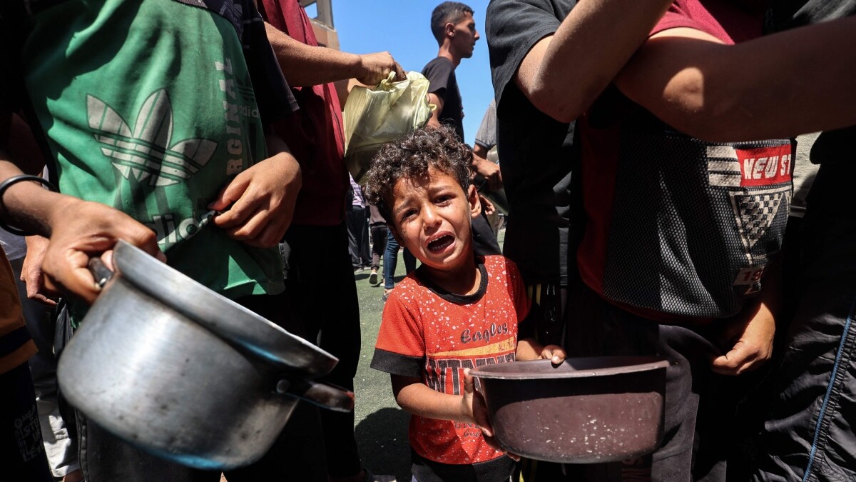 A child cries as Palestinians gather to receive a hot meal at a food distribution point in the Nuseirat camp in Gaza | AFP