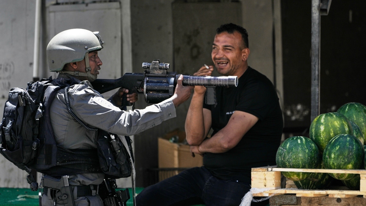 An Israeli border police officer takes up position next to a watermelon vendor, during a military raid | AP