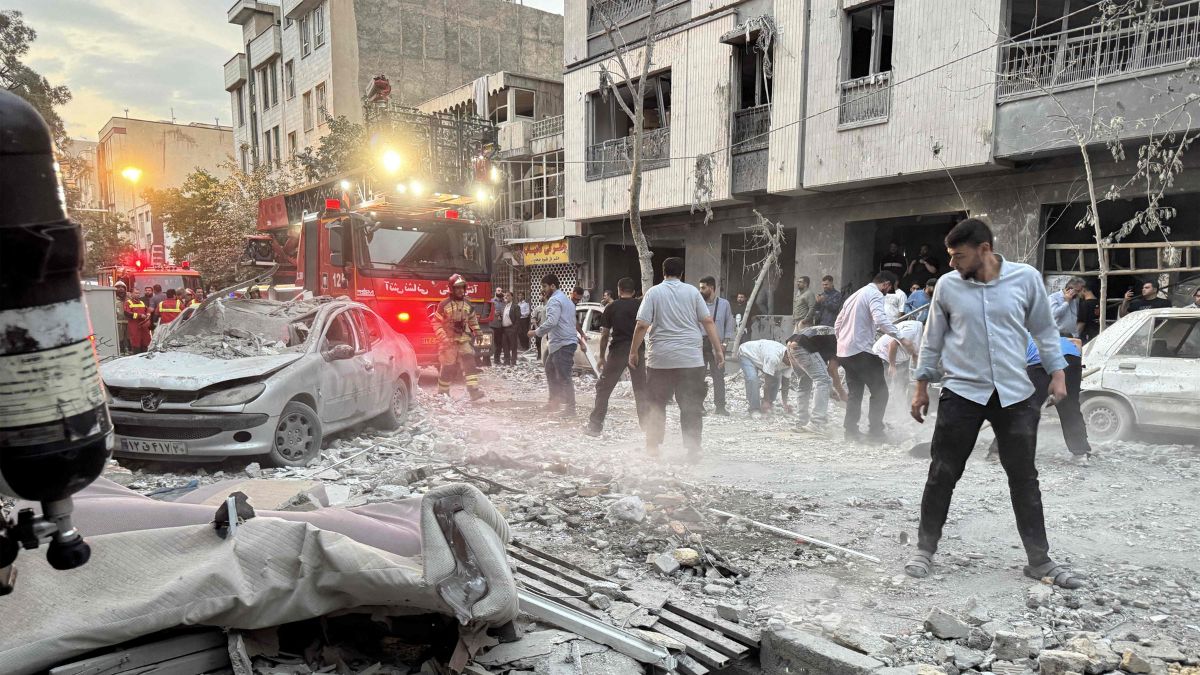 People and first-responders gather outside a that was hit by an Israeli strike in Tehran on June 13, 2025 | AFP