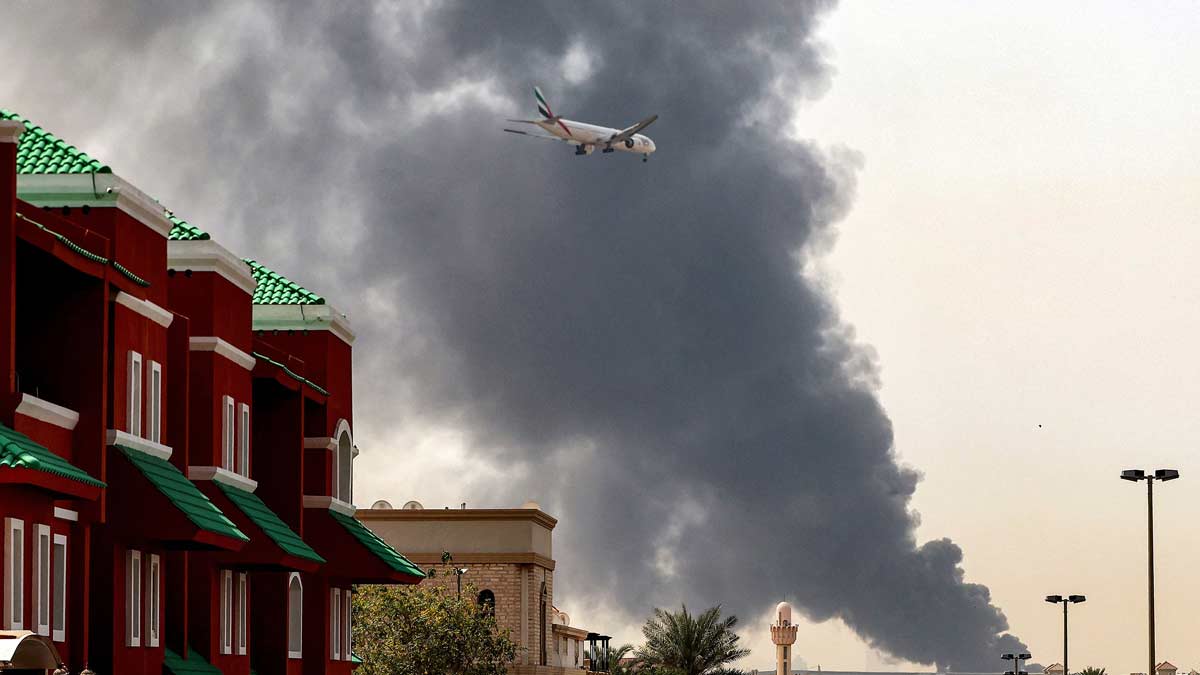 An Emirates aircraft prepares for landing as a smoke plume rises from an ongoing fire near Dubai International Airport in Dubai on March 16 | AFP