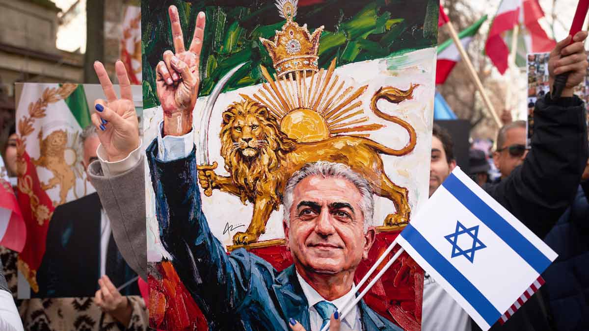 A member of the Iranian community flashes a victory sign from behind a poster of Iran's exiled crown prince Reza Pahlavi during a rally outside the Iranian embassy in Bucharest, Romania | AP