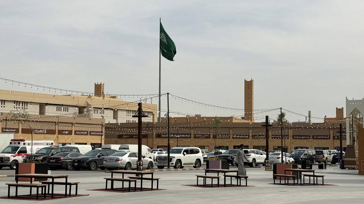 A man walks as a Saudi flag flutters in the background at Al Qaisareyah Market | Reuters