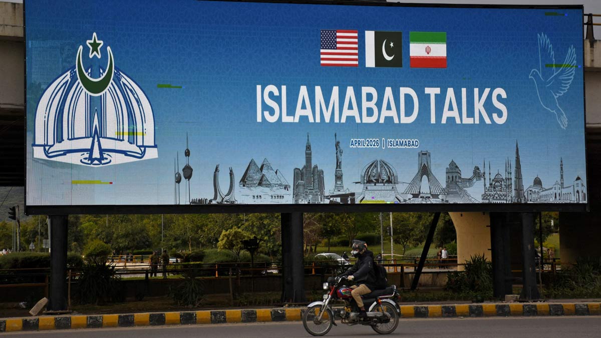 A man rides his motorbike past a billboard installed alongside a road as Pakistan prepares to host the US and Iran for peace talks, in Islamabad | Reuters
