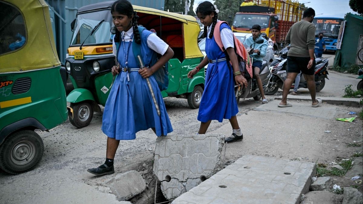 Children walk past broken slabs above road water drainage in Bengaluru | AFP