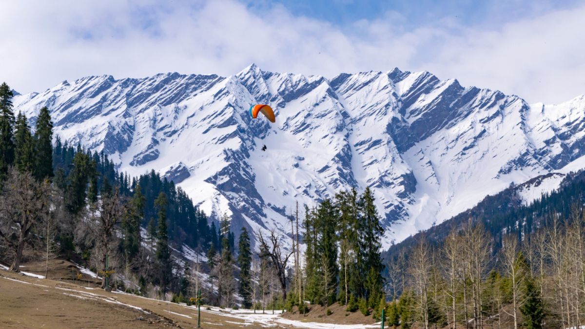 A tourist paraglides in Himachal Pradesh, with the Dauladhar peaks in the background