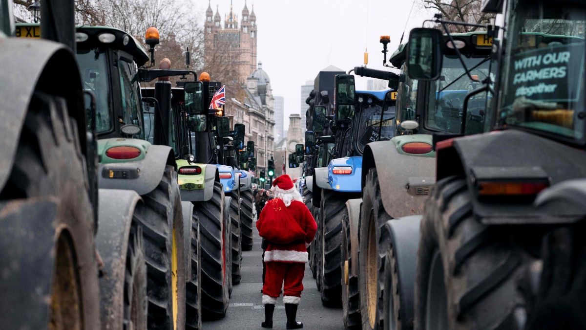 A person dressed as Santa Claus walks among tractors parked along Whitehall during a stop the death of British Farming demonstration | AFP