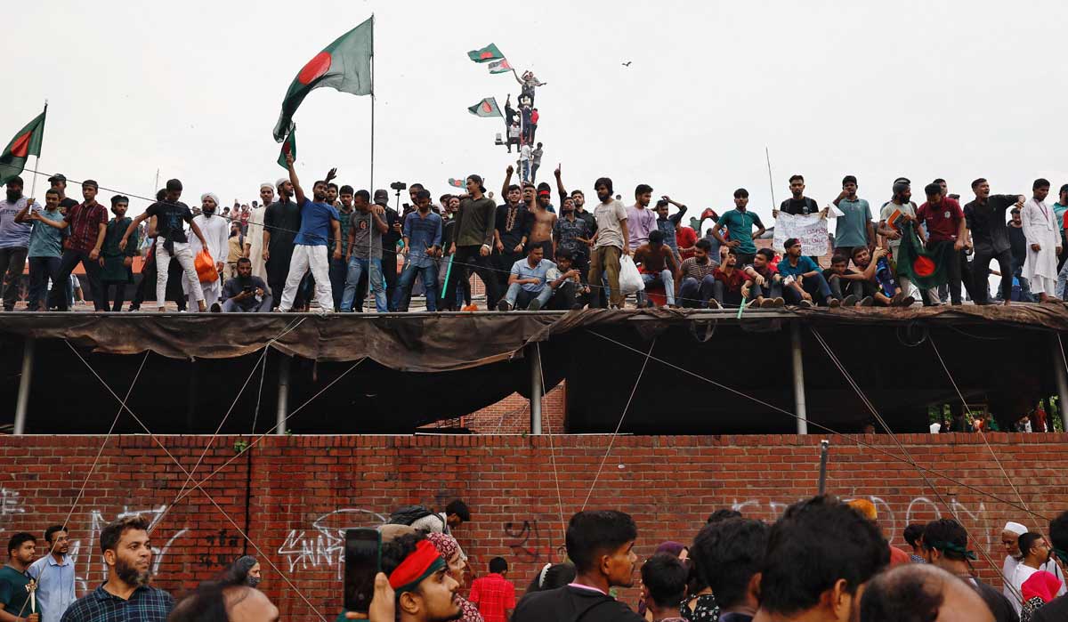 People waves Bangladeshi flags on top of the Ganabhaban, the Prime Minister's residence, as they celebrate the resignation of PM Sheikh Hasina in Dhaka, Bangladesh | Reuters