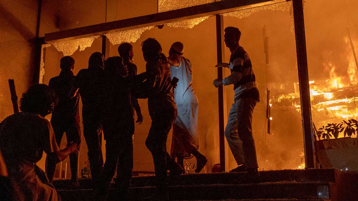 People are seen at the entrance to the Daily Star building as it burns in Dhaka amid protests following the news of the death of Sharif Osman Hadi | AFP